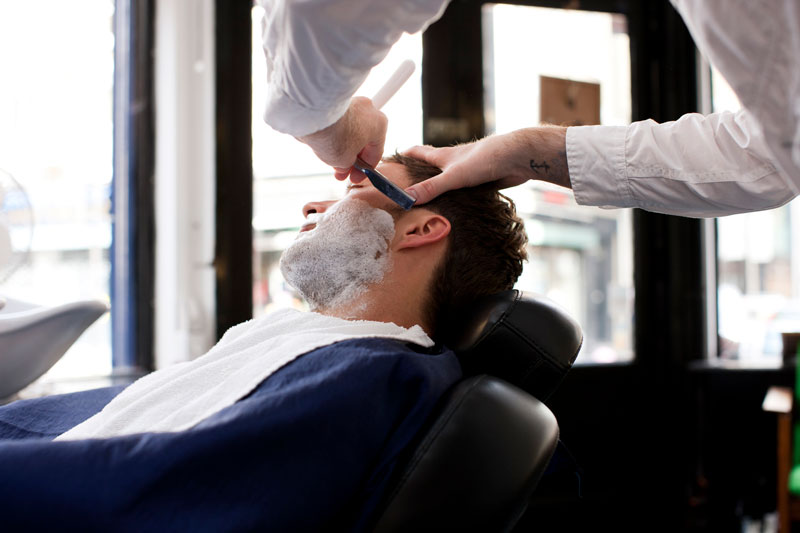 En man som får skägget fixat hos en barberare.