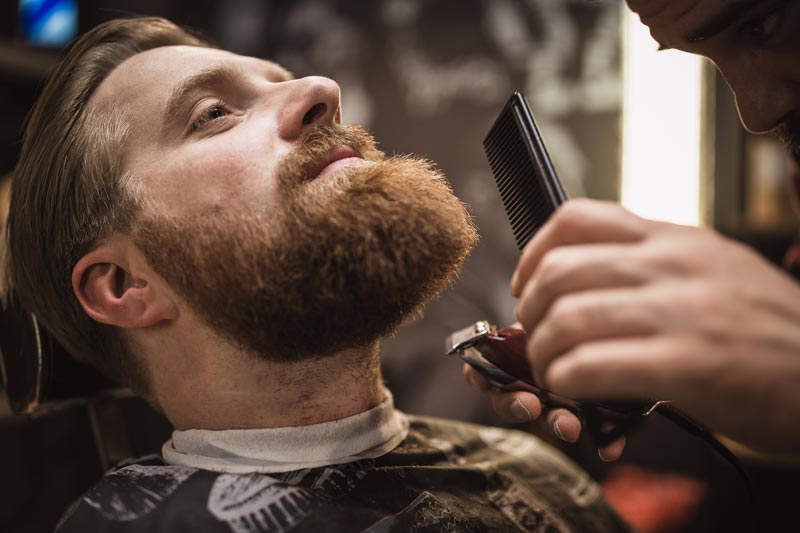 En man som får skägget fixat hos en barberare.